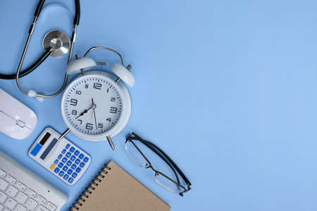 Flat lay composition with alarm clock, calculator and stethoscope on light blue background. Space for textの写真素材