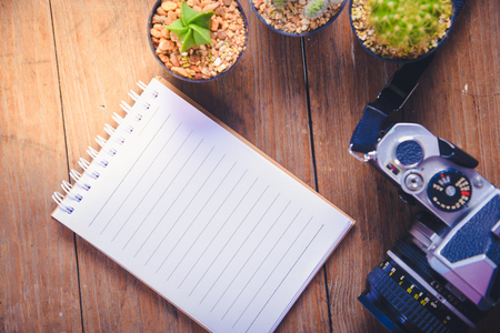 top view image of open notebook with blank pages and three cactus and camera  on wooden table..の写真素材