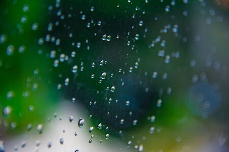 Drops of rain on glass with green tree nature background,romantic shot scene content,colorful raindrops.Blurred leaves of trees.の写真素材