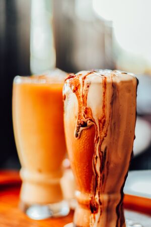 Iced coffee with milk, chocolate syrup being poured into it showing the texture on wood table.の写真素材