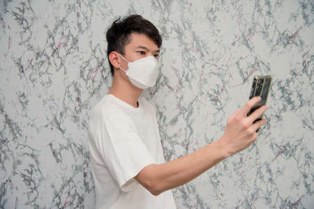 Man puts on a face mask using smartphone isolated on White background,pandemic and social distancing concept.Covid-19の写真素材