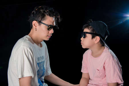 Man and little boy with sunglasses sit  on dark studio background , asian familyの写真素材