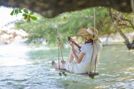 Beautiful woman playing ukulele under a tree by the sea.の写真素材