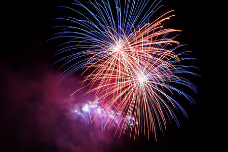 Red and blue celebratory fireworks in the night sky. Multi-colored fireworks display on black background.の写真素材