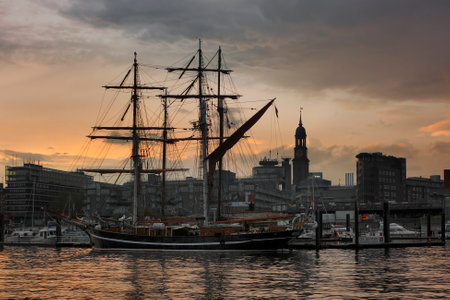 Hamburg, Germany - May 10, 2012: Sailboat 'Eye Of The Wind Gilleleje' in the harbor of Hamburg at beautiful sunset. Nightscape of the downtown and the tower of the church of St. Michaelis.のeditorial素材