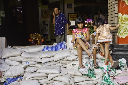BANGKOK - NOVEMBER 3: Although the possibility of the flood attack is almost everywhere in Bangkok, the children can still smile and play around even on the sandbags arrays.のeditorial素材