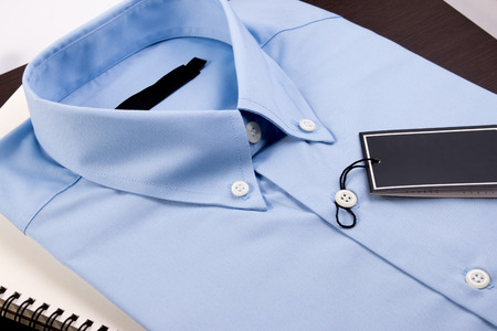 Blue shirt and notebook on wooden background. Blue shirt with black blank price tag on wooden table.の写真素材