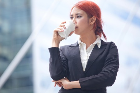 Portrait of young business asian woman standing with coffee in modern cityの写真素材