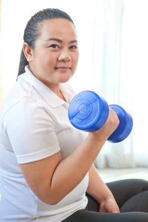 Young asian fat woman does fitness with dumbbell in homeの写真素材