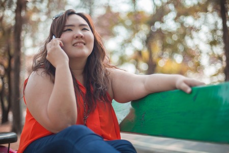 Happy fatty asian woman using mobile phone outdoor in a parkの写真素材