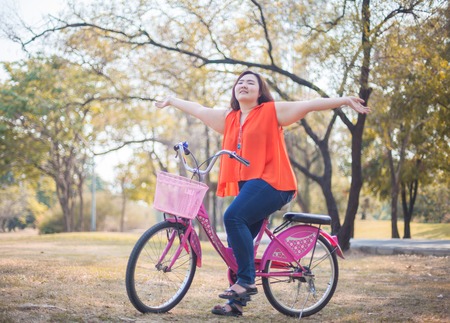 Happy fatty asian woman outstretched with bicycle outdoor in a parkの写真素材