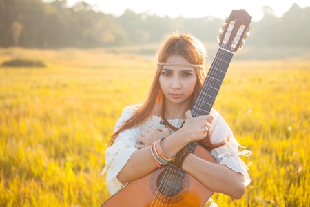 Hippie woman in golden field with acoustic guitarの写真素材
