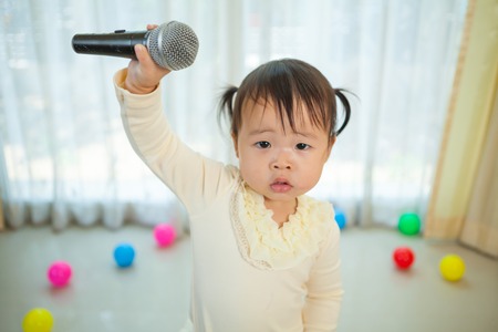 Happy little asian girl with microphone in the homeの写真素材