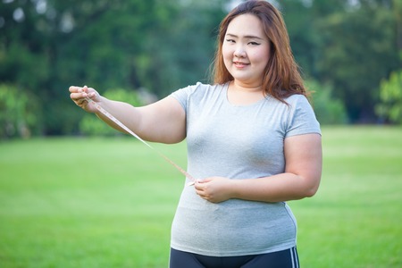 Happy fat asian woman measuring her stomach in the parkの写真素材