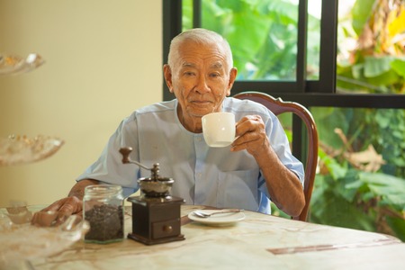 Asian senior man with vintage coffee grinder and coffee beansの写真素材