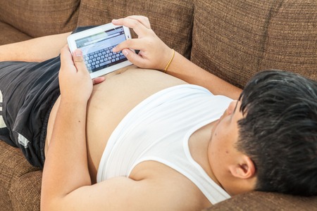 Asian fat man Relaxing in the sofa with the tablet at homeの写真素材