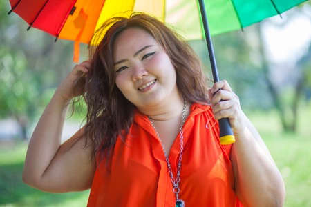 Happy fatty asian woman with umbrella outdoor in a parkの写真素材