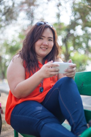 Happy fatty asian woman using mobile phone outdoor in a parkの写真素材