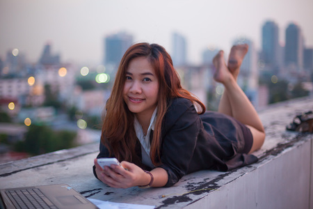 Asian woman using her mobile phone, city skyline night light backgroundの写真素材