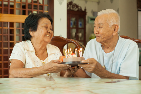 Asian senior couple holding a cake and smiling in living roomの写真素材