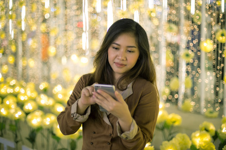 Outdoor portrait of beautiful young asian woman using her mobile phone at night.の写真素材