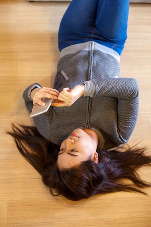 Happy asian young woman lying using smart phone at homeの写真素材