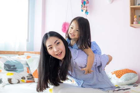 Happy little asian girl on the back of her mother in the houseの写真素材
