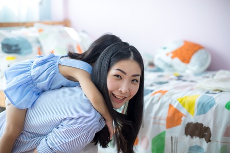 Happy little asian girl on the back of her mother in the houseの写真素材
