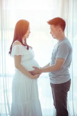 Young asian couple expecting baby standing together indoorsの写真素材