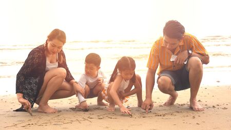 Young family of four sitting and play the sand on the beachの写真素材