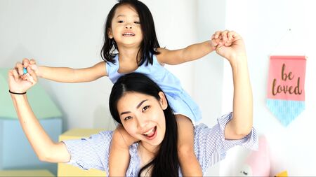 Happy little asian girl on the back of her mother in the houseの写真素材