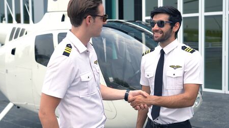 Portrait of commercial pilot in uniform standing near small private helicopter