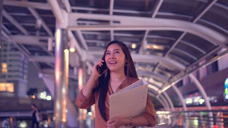 Beautiful business young asian woman walking in the night city streets using smartpone