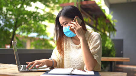 Asian woman talking by mobile phone working from home during Coronavirus or Covid-19 quarantine