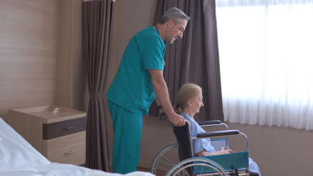 Doctor taking care of mature female patient sitting on wheelchair in hospitalの写真素材