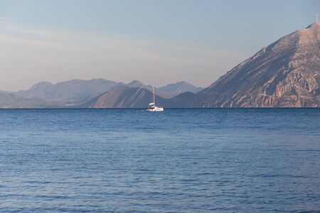 A mountain range in Greece with the ocean in the foreground and a sailing yacht.
