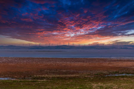 Photograph of large Wind Turbines during a cloudy sunset along a hill ridge line around Lake George...