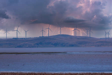 Photograph of large Wind Turbines in a row along a hill ridge line around a large lake during a...