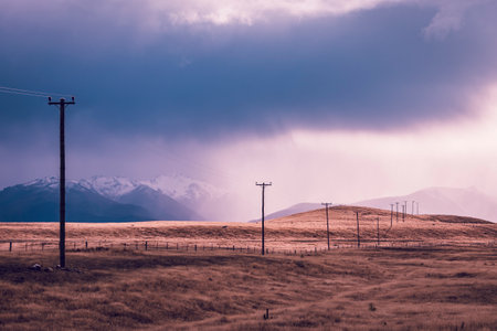 Photograph of telephone poles running through a valley against snow capped mountains on the South Island of New Zealandの写真素材