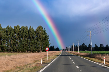 Photograph of a large rainbow over a regional road and agricultural field on the South Island of New Zealandの写真素材