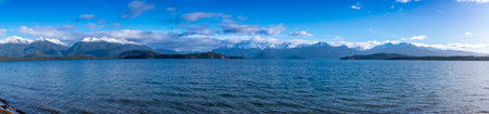 Photograph of a large blue lake and snow-capped mountain range while driving from Te Anau in...