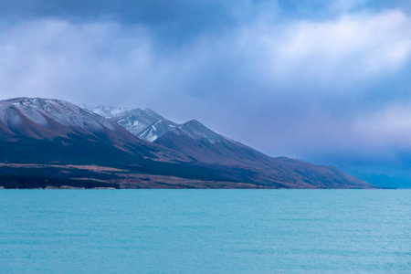 Photograph of Lake Pukaki early in the morning on a cloudy day with snow-capped mountains in the background on the South Island of New Zealandの写真素材