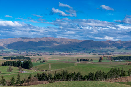 Photograph of a mountain range running behind a large green agricultural field with low level grey...