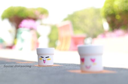 Social distancing concept with white smiley face on white flower pot in yellow mark on the cement floor,の写真素材