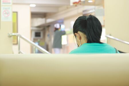 Back view of woman sitting on the chair in hospital for waiting to meet the doctor on blurred background of nurse at counterの写真素材