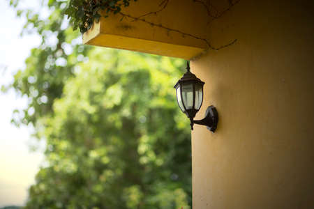 Retro and vintage black metal electric lantern on the yellow wall with blurred tree backgroundの写真素材