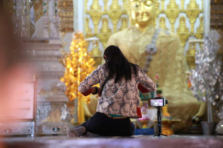 Women sitting on floor with mobile phone for take footage with blurred face of buddha, Travelling people with mobile phone or camera for record activityのeditorial素材