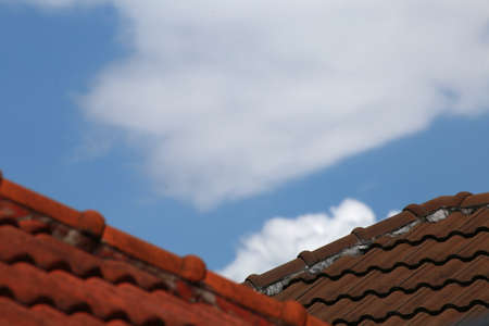 Old red brick roof tiles on blue sky and white cloud background, selective focusの写真素材