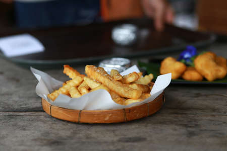 Close up french fries with salt in white paper and wooden tray put on wood table in restaurant, selective focusの写真素材