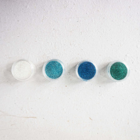 Blue and turquoise glitter in clear jars on white background.の写真素材